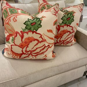 May include: Three decorative throw pillows with a floral pattern in shades of red, green, and orange on an off-white background. The pillows are placed on a light-colored sofa, creating a cozy and inviting atmosphere.