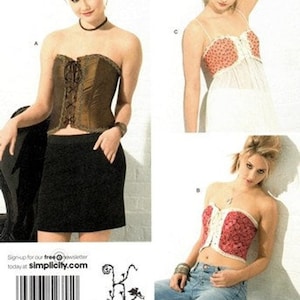 May include: Simplicity sewing pattern featuring three different corset designs. One corset is brown with lace-up detailing, another is red with white trim, and the third is white with a floral pattern. The pattern includes a black skirt and jeans.