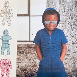 May include: A sewing pattern for a hooded jumpsuit for a child. The pattern includes three different variations: a blue jumpsuit with a zipper, a pink jumpsuit with hearts, and a blue jumpsuit with a zipper and a white stripe down the front. The pattern is for sizes 1/2-4.