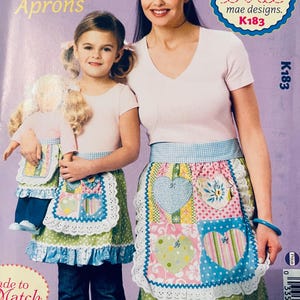 May include: A sewing pattern for two patchwork aprons, one for a child and one for an adult. The aprons are made of colorful fabric with hearts and other designs. The pattern is called "Pretty Patchwork Aprons" and is from "ellie mae designs."