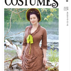 May include: A woman wearing a brown dress with a green bow and a green hat. The dress has a ruffled skirt and a fitted bodice. The woman is standing in a forest setting. McCall's Costumes M8189 Size A5 (6-8-10-12-14)