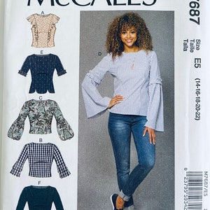 May include: McCall's sewing pattern M7687. The pattern features several blouse designs, including a striped top with bell sleeves. The size is E5, fitting sizes 14-22. The image also shows a woman wearing a striped blouse and jeans.