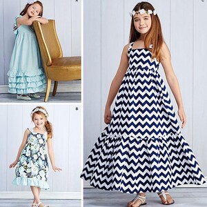 May include: Simplicity pattern 1121 features three girls' dresses. One dress is light blue with ruffled tiers, another has a floral print, and the third has a navy and white chevron pattern. The dresses are designed and printed in the USA.
