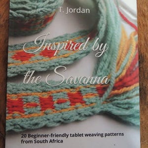May include: A book cover with the title "Inspired by the Savanna" featuring a teal woven design with red and yellow accents. The author's name, T. Jordan, is at the top. The cover also states "20 Beginner-friendly tablet weaving patterns from South Africa."