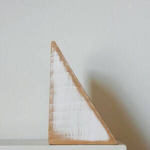 May include: A wooden triangle with a distressed white paint finish. The geometric shape is set against a neutral background, showcasing the natural wood grain and texture. The triangle is approximately 15 cm tall.