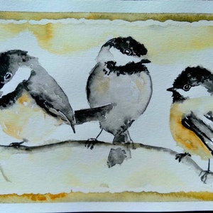 May include: Watercolor painting of three black-capped chickadees perched on a branch. The birds are painted in shades of gray, black, and white, with hints of yellow on their bellies. The background is a soft wash of yellow and white.