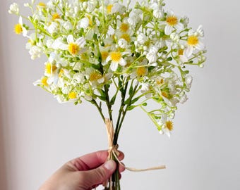 May include: A bouquet of white and yellow artificial flowers with green stems tied together with twine.