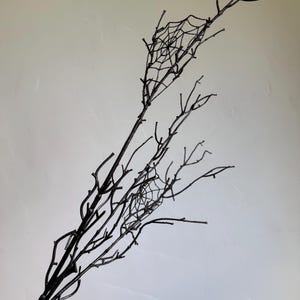 May include: A decorative black branch featuring multiple thin, twig-like stems extending outward. Two distinct, intricate spider web patterns are attached between the branches, creating a detailed, dark, and branching structure throughout the piece.