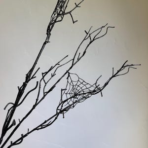 May include: A set of black decorative branches featuring thin, twig-like structures and a small, intricate spider web design attached to one of the branches. The branches are dark, slender, and have multiple offshoots extending in various directions.