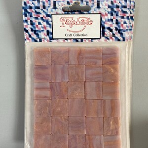 May include: A package of 25 pink and gold iridescent glass mosaic tiles. The tiles are square and have a swirled pattern. The package is labeled "Fine Style Craft Collection".