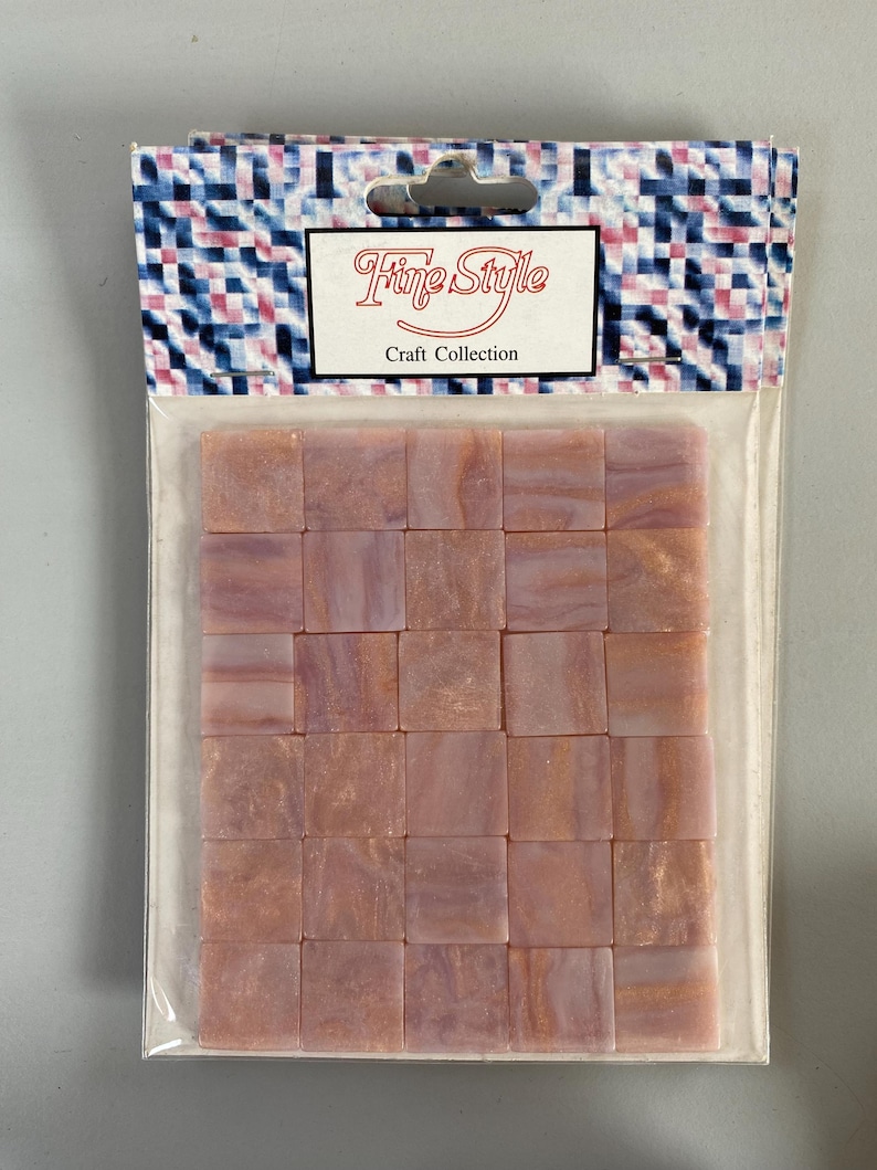 May include: A package of 25 pink and gold iridescent glass mosaic tiles. The tiles are square and have a swirled pattern. The package is labeled "Fine Style Craft Collection".