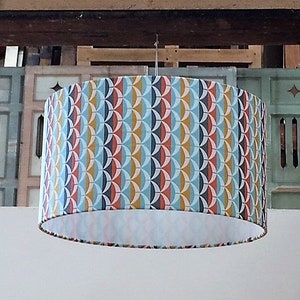 May include: A round, white lampshade with a geometric pattern in shades of blue, red, yellow, and black.