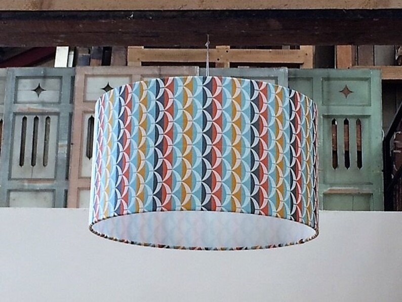 May include: A round, white lampshade with a geometric pattern in shades of blue, red, yellow, and black.