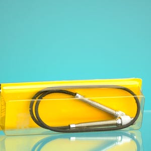 Può includere: Un accessorio per fotocamera Nikon, probabilmente un cavo di scatto remoto, confezionato in un contenitore di plastica giallo e trasparente. Il cavo è nero, con un connettore in metallo argentato. La confezione ha il logo Nikon.