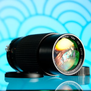 May include: A black camera lens with a silver ring and the text "MC AUTO ZOOM" and "Alsear 400" printed on the side. The lens is reflecting a colourful image.