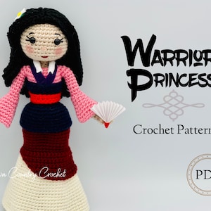 May include: Crochet pattern for a warrior princess doll. The doll is wearing a pink and red dress with a white fan. The pattern is available as a PDF download.