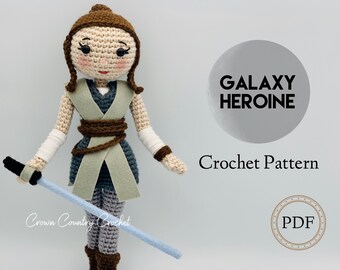 May include: Crochet pattern for a galaxy heroine, a crocheted doll with brown hair, a light blue lightsaber, and a grey and brown outfit. The pattern is available as a PDF download. The text on the image reads "Galaxy Heroine Crochet Pattern PDF".