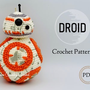 May include: Crochet pattern for a droid, a white and orange character with a black eye. The pattern is available as a PDF download. The image also includes the text "DROID Crochet Pattern".