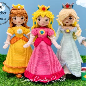 Peut inclure: Trois poupées en crochet habillées en princesses. Les poupées portent des robes jaunes, roses et bleues avec des couronnes. Les poupées sont debout sur une surface herbeuse verte avec un ciel bleu en arrière-plan. Le texte "PDF Crochet Pattern" est dans une couronne en haut à gauche de l'image.