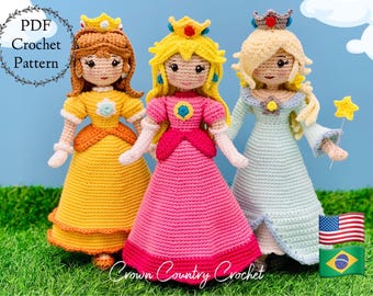 May include: Three crocheted dolls dressed as princesses. The dolls are wearing yellow, pink, and blue dresses with crowns. The dolls are standing on a green grassy surface with a blue sky in the background. The text "PDF Crochet Pattern" is in a wreath at the top left of the image.