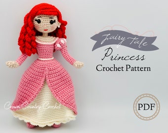 May include: Crochet pattern for a fairy tale princess doll. The doll is wearing a pink dress with a white underskirt and has long red hair. The pattern is available as a PDF download. "Fairy Tale Princess Crochet Pattern" and "PDF" are written on the image.