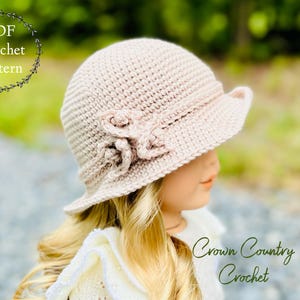 May include: A light beige crochet hat with a small brim and a decorative flower. The hat is part of a PDF crochet pattern. The text "PDF Crochet Pattern" and "Crown Country Crochet" are visible in the image.