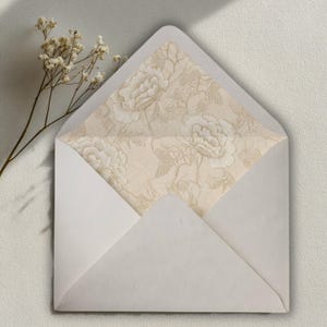 May include: A white envelope with a floral patterned interior. The interior features a cream-colored design of large flowers and foliage. A sprig of dried flowers is visible to the left of the envelope.