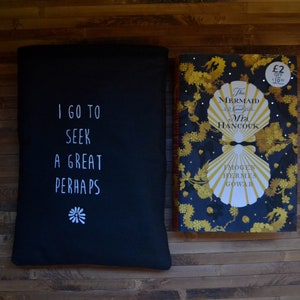 Pode incluir: Uma capa de livro preta com o texto "I GO TO SEEK A GREAT PERHAPS" e um desenho de flor branca. Ao lado, um livro intitulado "The Mermaid of Black Conch" com capa azul marinho e detalhes dourados.