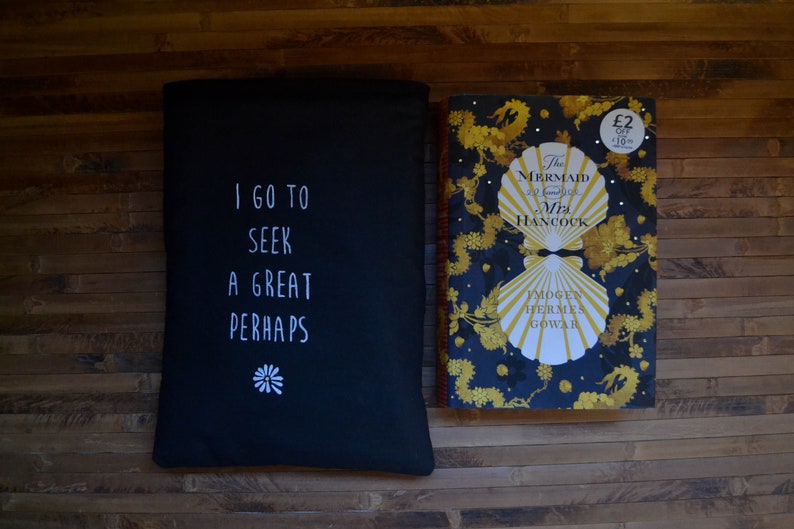 Pode incluir: Uma capa de livro preta com o texto "I GO TO SEEK A GREAT PERHAPS" e um desenho de flor branca. Ao lado, um livro intitulado "The Mermaid of Black Conch" com capa azul marinho e detalhes dourados.
