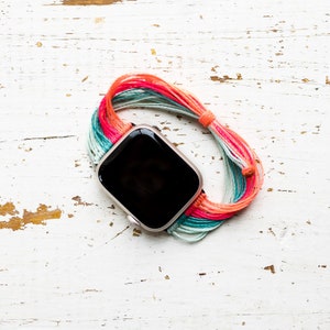 May include: A smartwatch with a black face and a colorful woven band. The band is made of multiple strands of yarn in shades of pink, blue, and green.