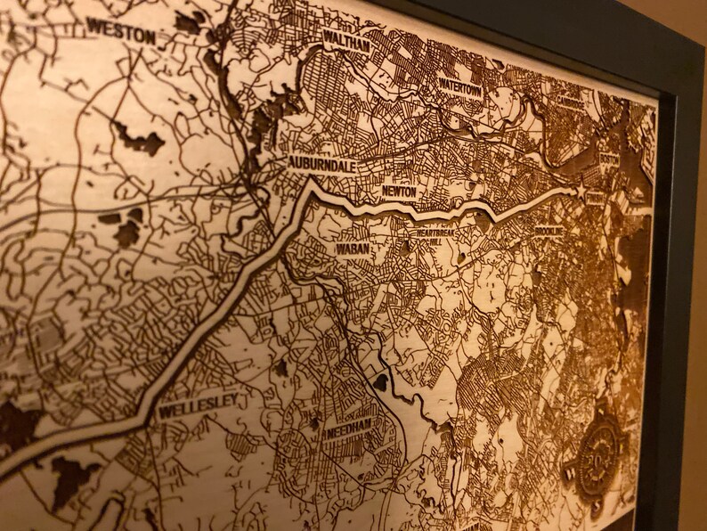 May include: A laser-engraved wooden map of the Boston area, showing the towns of Weston, Waltham, Watertown, Auburndale, Newton, Waban, Wellesley, and Needham. The map is framed in a black frame.