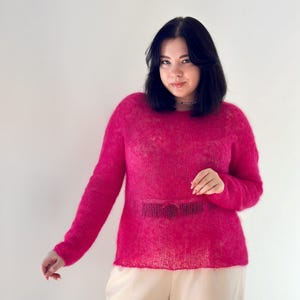 May include: A woman wearing a pink fluffy sweater and beige trousers.