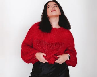 Könnte beinhalten: Eine Frau trägt einen roten Strickpullover und einen schwarzen Satinrock. Sie schaut nach oben und lächelt.
