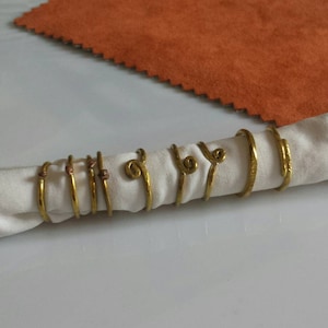 Puede incluir: Un juego de seis anillos de servilleta de metal dorado con un diseño retorcido. Los anillos están dispuestos sobre una servilleta blanca.