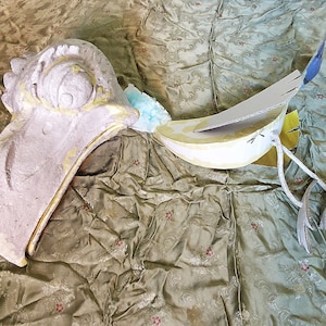 Könnte beinhalten: Eine teilweise zusammengesetzte Vogelskulptur aus Papiermaché mit einem Körper und Flügeln aus Pappe. Der Vogel ist weiß mit goldenen Akzenten bemalt und hat eine blaue Schwanzfeder.