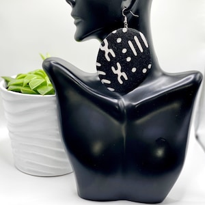 May include: Black and white patterned round wooden earrings. The earrings are large and have a geometric design.