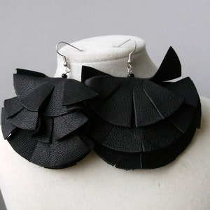 May include: A pair of black leather earrings with a layered, ruffled design. The earrings are hanging from silver hooks.