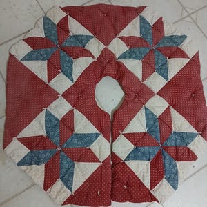 May include: A circular quilted tree skirt featuring a patchwork star pattern in red, cream, and blue. The fabric displays a small white dot print on the red sections, a floral pattern on the blue star points, and a cream background with tiny dots.