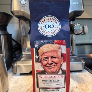 May include: A bag of Republican Coffee Company Trump Roast medium roast ground coffee. The packaging features a portrait of Donald Trump against an American flag background, with the text "Republican Coffee Company," "Trump Roast," "Medium Roast," "Roasted in Florida," and "Net Wt 12oz (340g)."