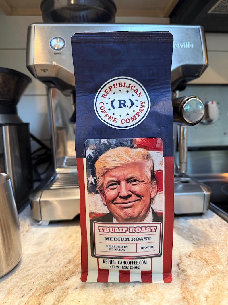 May include: A bag of Republican Coffee Company Trump Roast medium roast ground coffee. The packaging features a portrait of Donald Trump against an American flag background, with the text "Republican Coffee Company," "Trump Roast," "Medium Roast," "Roasted in Florida," and "Net Wt 12oz (340g)."