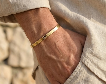 Puede incluir: Una pulsera rígida de metal en tono dorado con un acabado liso y pulido y una banda fina y plana. La superficie exterior de la pulsera está grabada con el texto en cursiva "To be, rather than to seem."