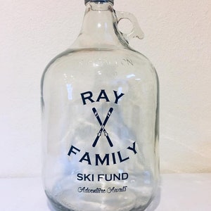 K&ouml;nnte beinhalten: Ein klares Glasgef&auml;&szlig; mit schwarzem Deckel und Henkel. Das Gef&auml;&szlig; hat ein schwarz-wei&szlig;es Design mit der Aufschrift "Ray Family Ski Fund Adventure Awaits".