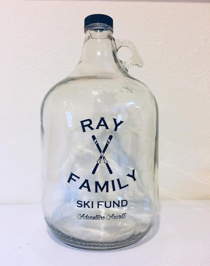 K&ouml;nnte beinhalten: Ein klares Glasgef&auml;&szlig; mit schwarzem Deckel und Henkel. Das Gef&auml;&szlig; hat ein schwarz-wei&szlig;es Design mit der Aufschrift "Ray Family Ski Fund Adventure Awaits".