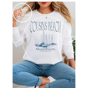 Puede incluir: Sudadera blanca con el texto "COUSINS BEACH" en escritura azul oscuro. Debajo, un gráfico de veleros y las palabras "Massachusetts Population 848" en azul a juego. Descarga digital.