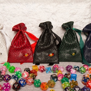 A selection of pocket-sized dice bags made of faux leather with a dragon style texture and an eyeball embedded in the front - available in white, red, black, green and blue.