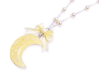 May include: A delicate silver chain necklace with a crescent moon pendant. The moon is yellow with a glittery finish and white stars. The necklace also features white pearl beads and silver star charms.