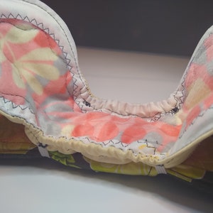 May include: A close-up of the inside of a cloth nappy. The nappy is made of a soft, absorbent material and has a colourful floral print. The nappy is open and the inside is visible, showing the layers of fabric.
