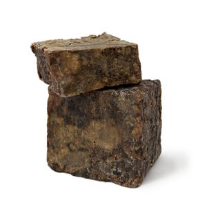 May include: Two bars of dark brown African black soap stacked on top of each other. The soap has a rough, textured surface.
