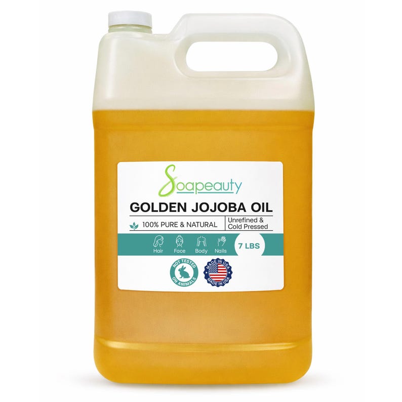 May include: A large, clear plastic jug filled with golden jojoba oil. The label reads "Soapeauty GOLDEN JOJOBA OIL 100% PURE & NATURAL" and lists uses for hair, face, body, and nails. The jug contains 7 lbs of oil.