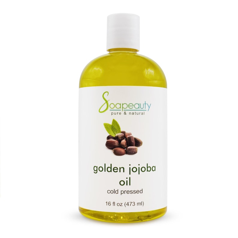 May include: A bottle of golden jojoba oil from Soapeauty. The label features the brand name, a graphic of jojoba beans and leaves, and the text "golden jojoba oil, cold pressed, 16 fl oz (473 ml)." The bottle has a white cap.